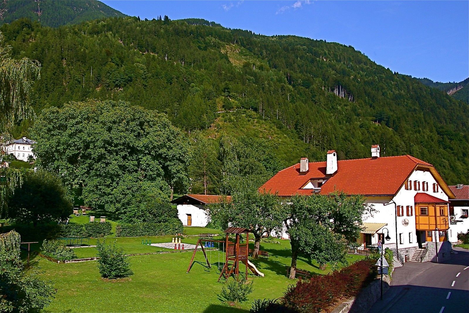 Außenansicht des Spiele- und Buchhotels Tschitscher mit rotem Dach, Garten und kleinem Spielplatz, im Grünen gelegen